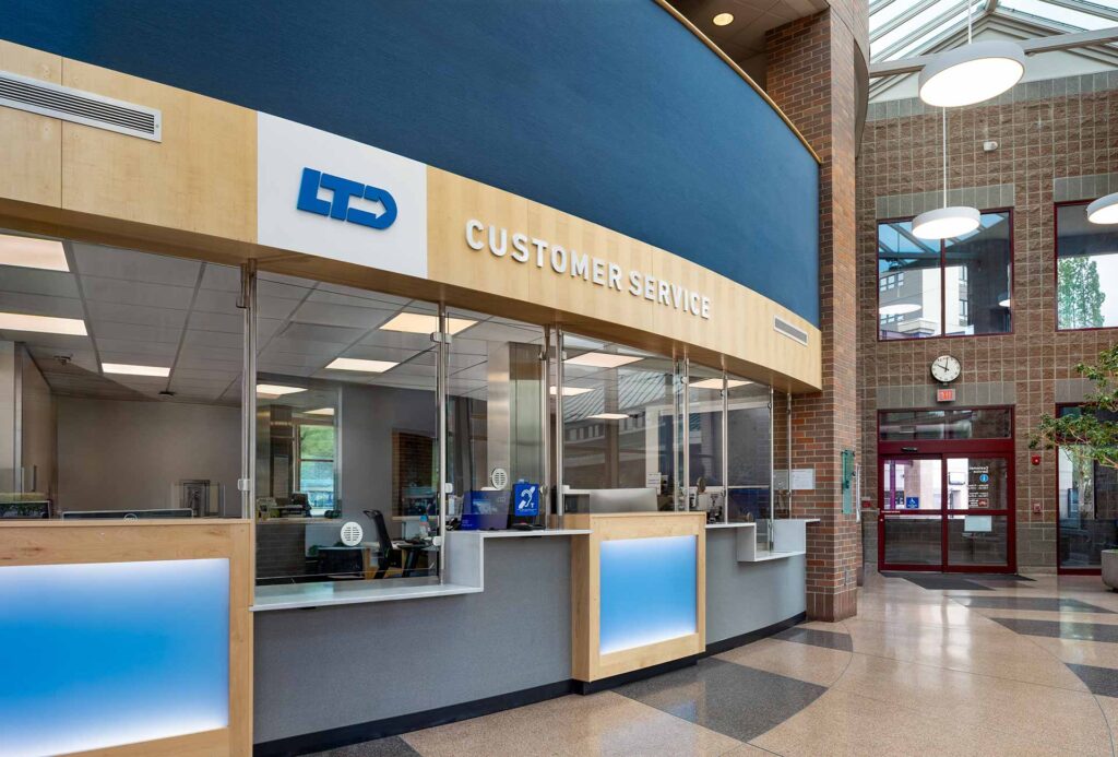 Customer service counter in a spacious, modern building lobby with glass windows, a clock, and multiple service stations.