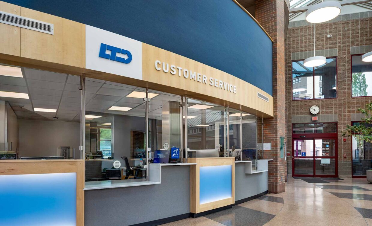 Customer service counter in a spacious, modern building lobby with glass windows, a clock, and multiple service stations.