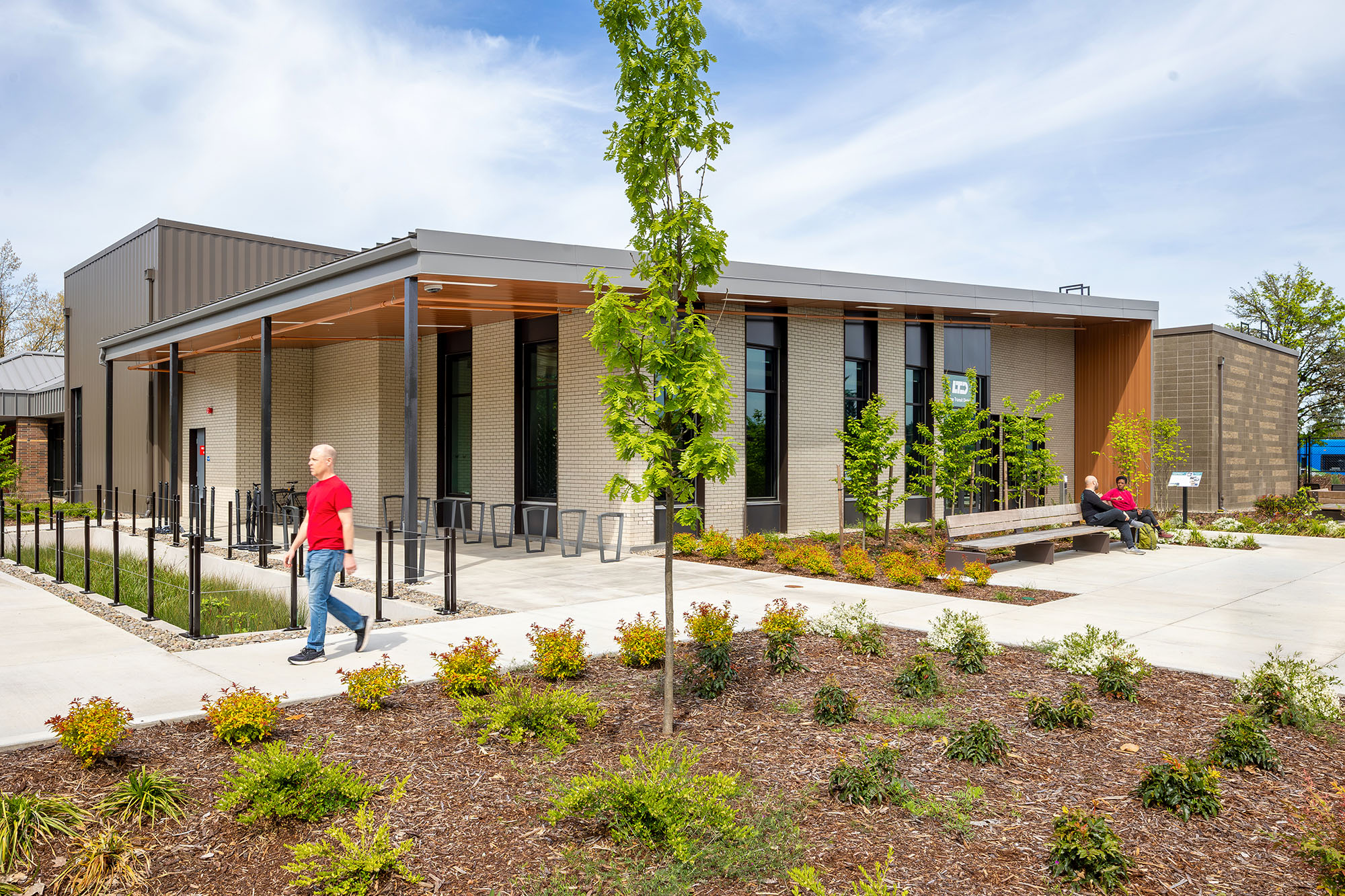 A modern, single-story building with large windows and a covered entrance; landscaped grounds and a few people outside on a sunny day.