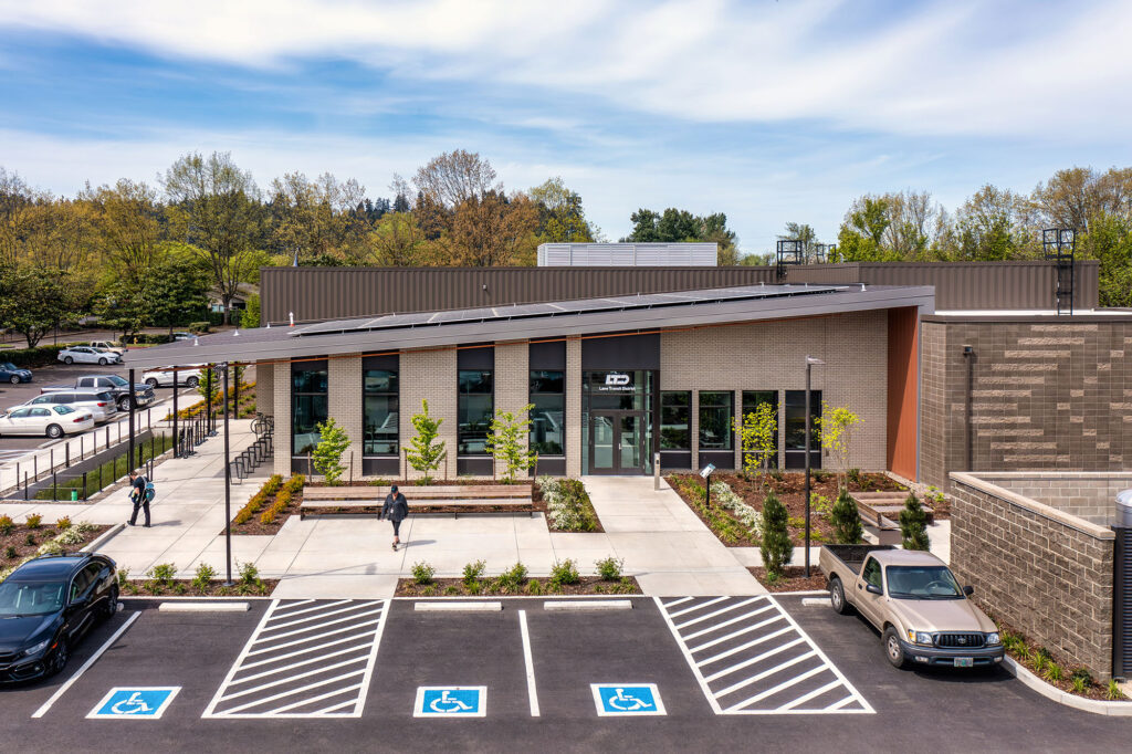 Modern single-story building with large windows, landscaping, and accessible parking spaces in front; a few people are walking near the entrance.