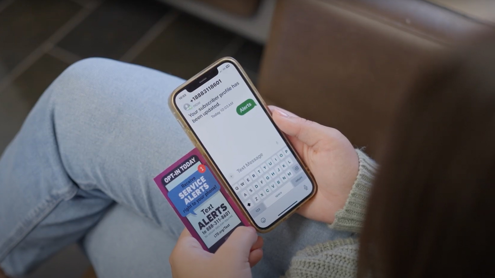 A person holding a mobile phone and a service alerts card, typing a text message to receive alerts.