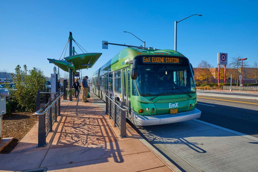 A green EmX bus is stopped at a station where a few people are boarding on a clear day; a Target store is visible in the background.
