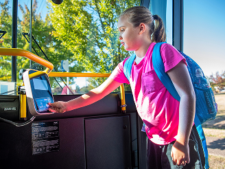 product1 A young girl with a blue backpack taps a card on a contactless payment reader while boarding a bus on a sunny day.