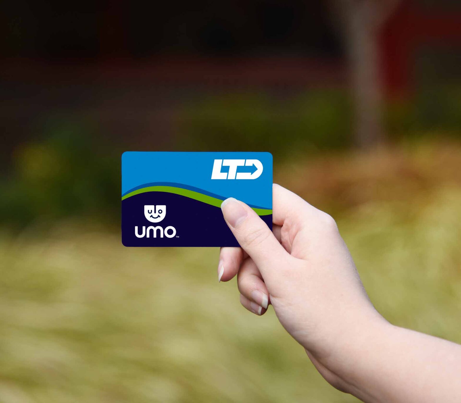 A hand holds an LTD Umo transit card against a blurred outdoor background with greenery.