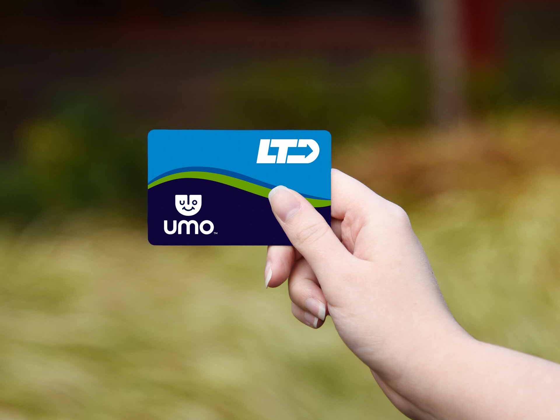 A hand holds an LTD Umo transit card against a blurred outdoor background with greenery.
