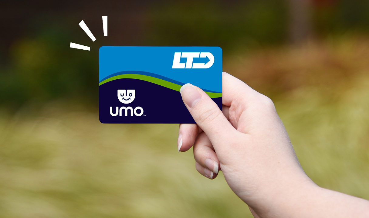 A hand holds an LTD Umo transit card outdoors, with a blurred green background.