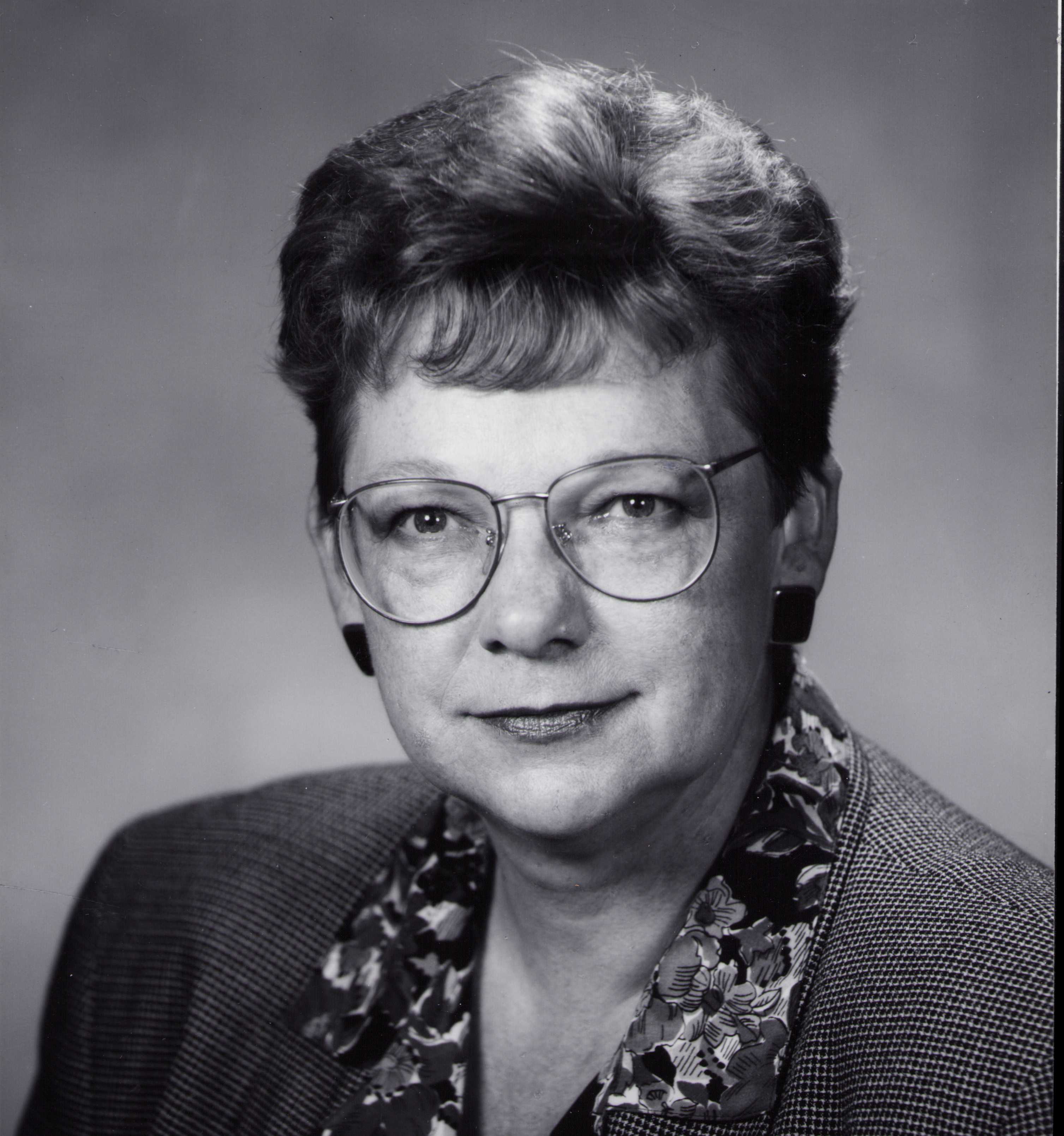 Black and white portrait of Phyllis Loobey with short hair, glasses, and a patterned blouse under a blazer, looking directly at the camera.