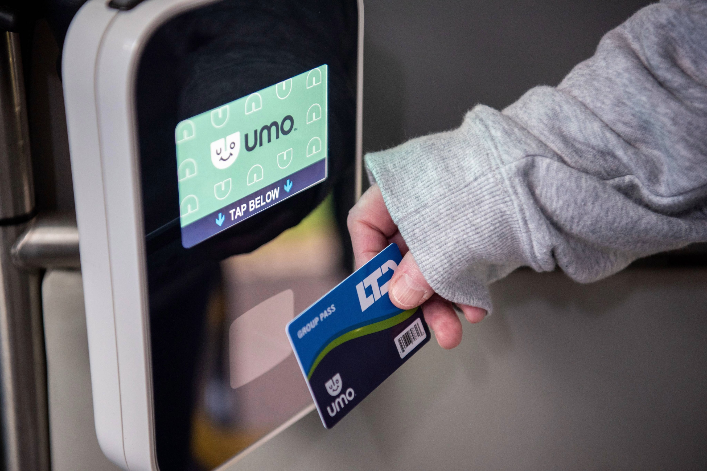 A person holds a Umo Group Pass card and taps it on a Umo fare reader for public transit access.