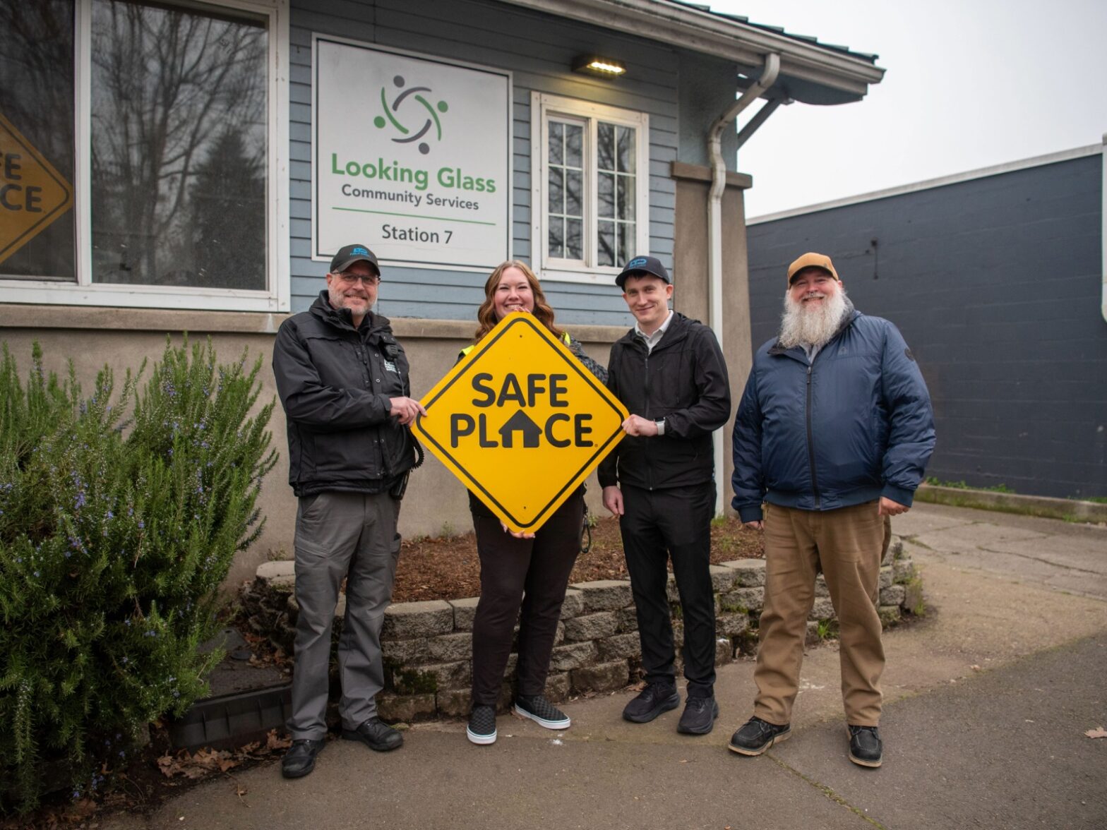 Four people stand in front of a building labeled "Looking Glass Community Services," holding a yellow "Safe Place" sign.