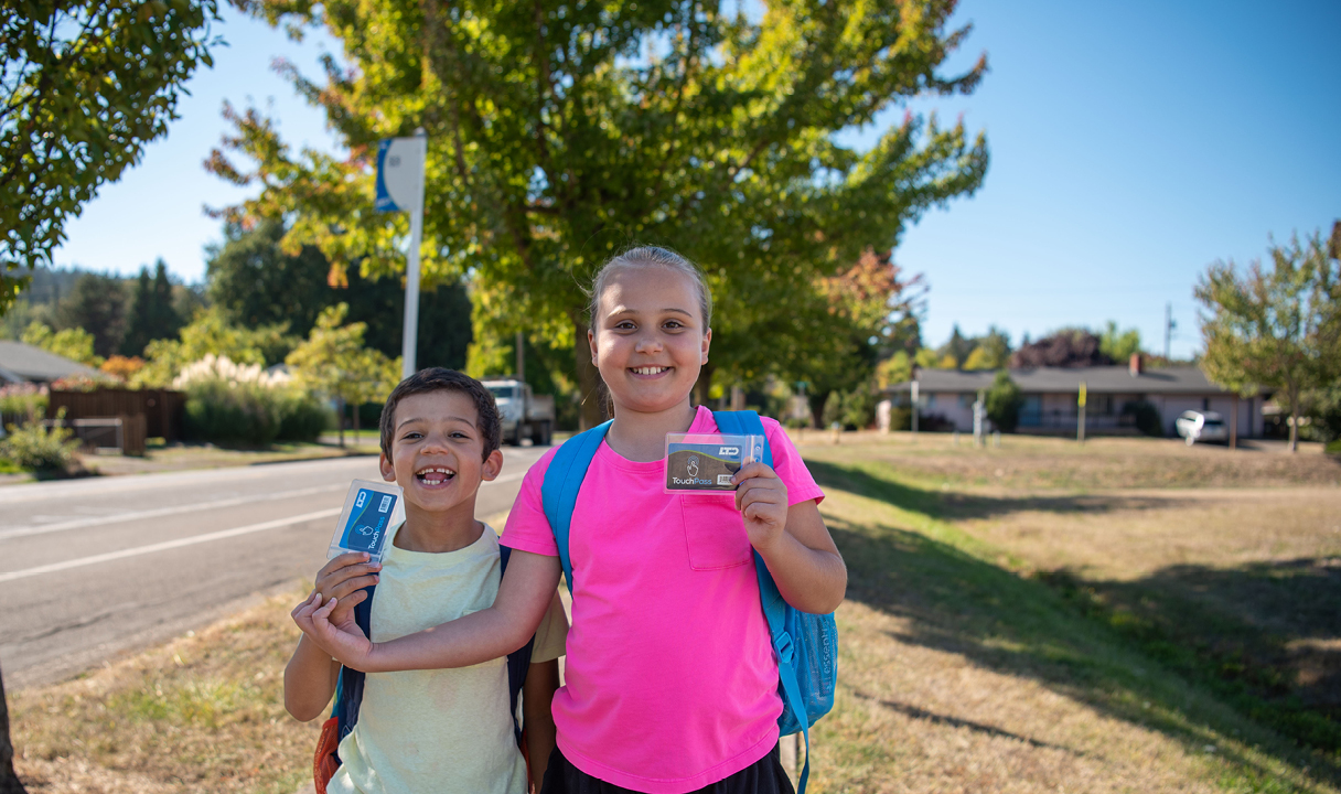Two children with backpacks hold up their transit passes.