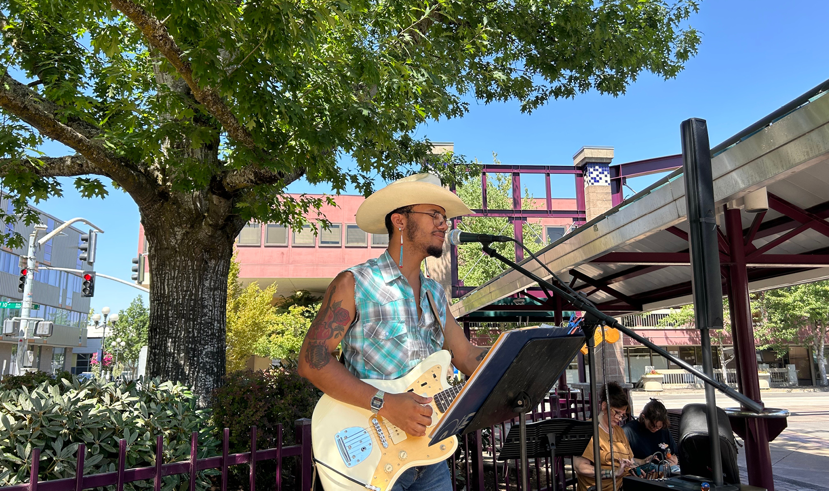 A performer playing electric guitar and singing at Eugene Station outdoors on a sunny day.