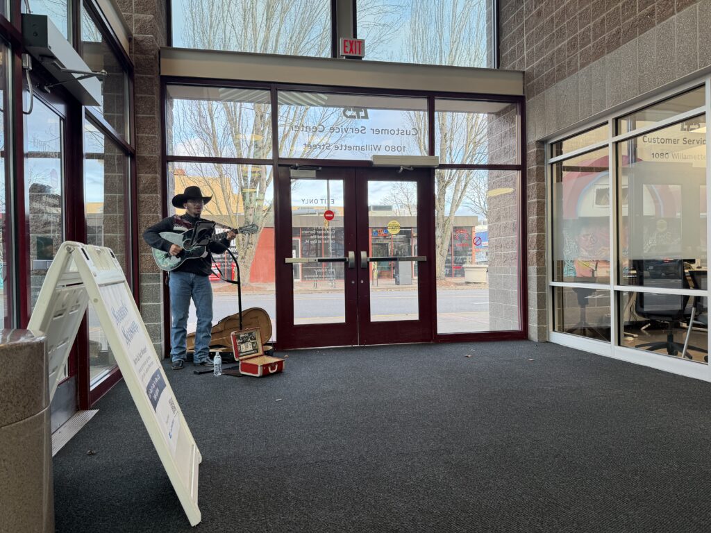 A man in a cowboy hat plays an acoustic guitar while standing in a building entrance.
