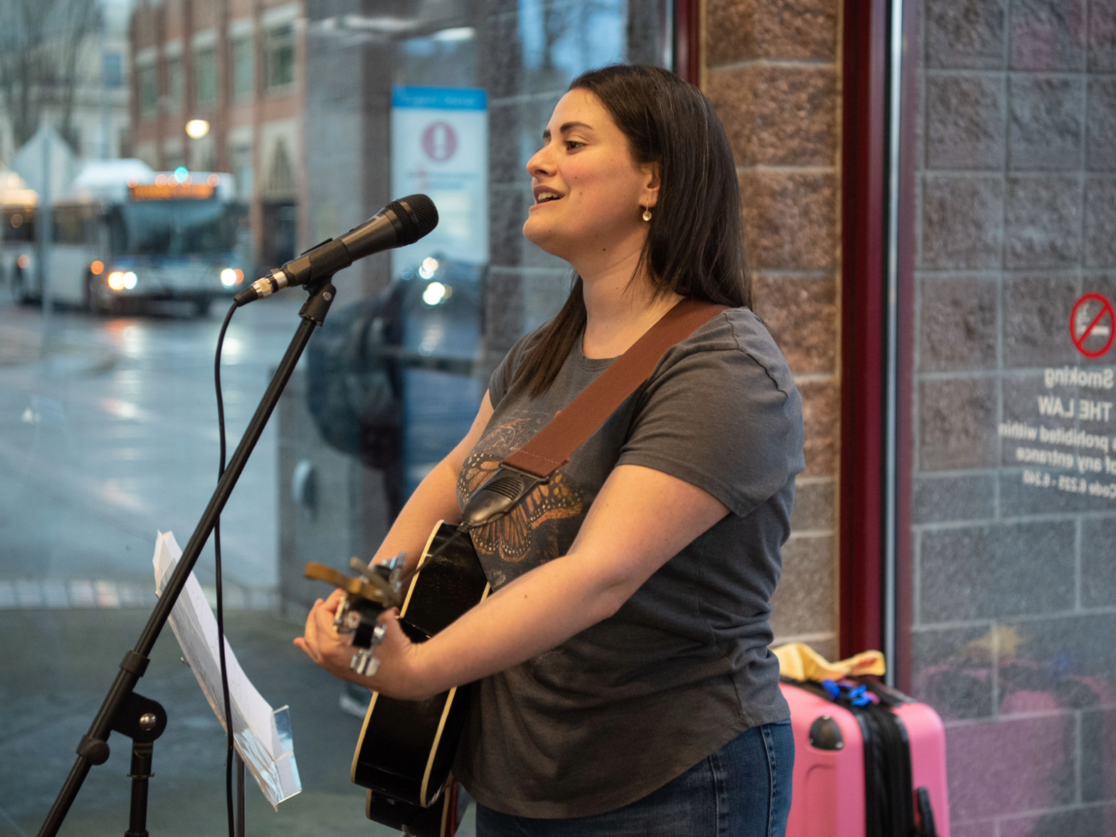 A woman singing into a microphone while playing an acoustic guitar.